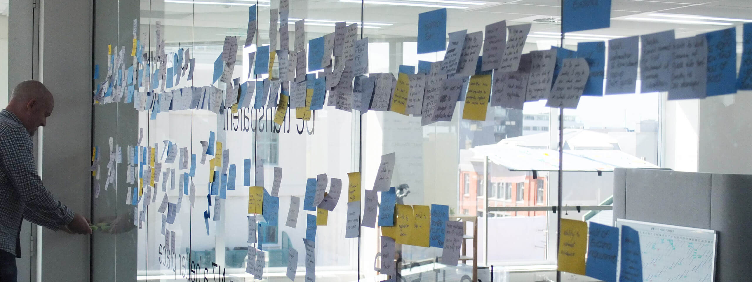 A project discovery workshop facilitator places post-its on a wall during user story mapping.