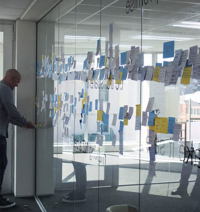 A project discovery workshop facilitator places post-its on a wall during user story mapping.