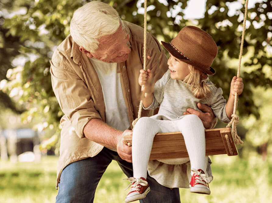A senior pushes his granddaughter on a swing while they enjoy an outing together.